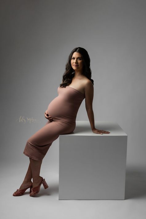 Modern maternity photoshoot of a pregnant woman wearing a strapless jersey knit gown as she leans against a white cube and rests on her right arm taken in a studio near Midtown in Atlanta, Georgia by Lily Sophia Photography. White Box Photoshoot, Maternity Photoshoot Studio, Studio Maternity Shoot Sweater, In Studio Maternity Session Dress, Minimalist Maternity Shoot Studio, Classic Studio Maternity Photos, Studio Maternity Shoot Gown, Maternity Studio Photoshoot, Knit Gown