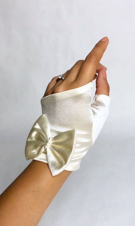 "Cute and dainty fingerless 1970s deadstock sating gloves that come in ivory or white. These gloves feature a sleeve for the thumb for flexibility and large bow at the wrist with pearl accent. Gloves have a lot of stretch and are intended to fit all sizes. Perfect for vintage brides; elopements, city hall weddings or big parties! Add extra flair to your outfits. These gloves would work well with those who want to show off their ring collections. Comes in original packaging. Measurements: Length: Ivory Gloves, City Hall Weddings, Silk Gloves, Satin Gloves, Sustainable Wardrobe, Gloves Vintage, Vintage Brides, Formal Gloves, Gloves Design