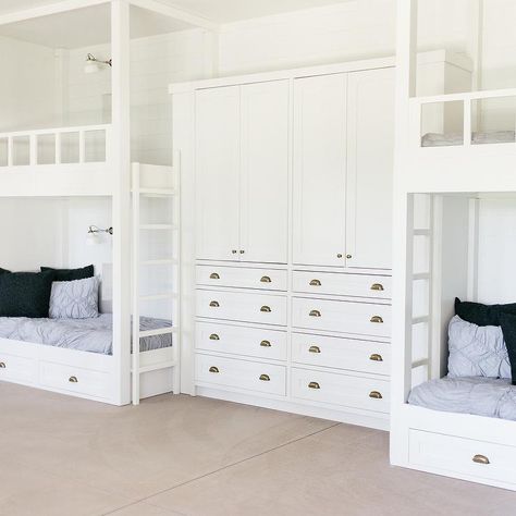 White built-in wardrobe cabinets adorned with brass cup pulls are fixed between white bunk beds positioned against as white shiplap trim and lit by white vintage sconces mounted over blue pin tuck bedding. Bunk Beds With Privacy, Bed Between Wardrobes, Girls Bunk Room, Bunk Bed Designs For Teens, Bunk Bed With Storage, Modern Bunk Beds, White Bunk Beds, Bunk Beds Built In, Brass Cup