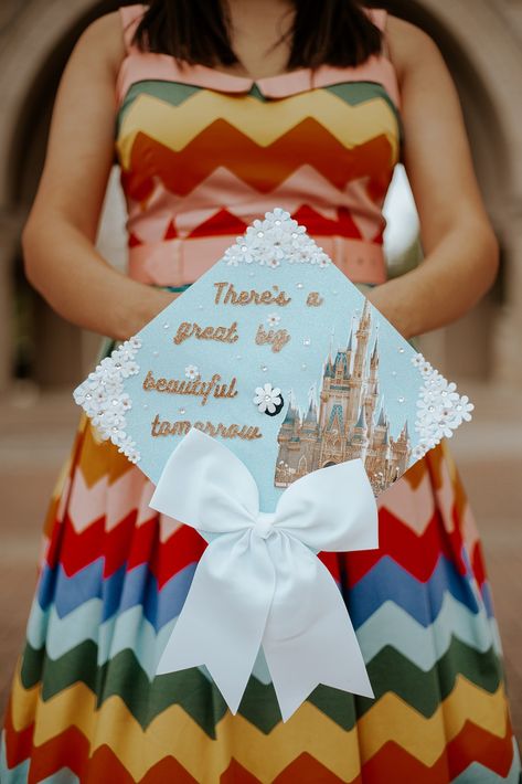 Sparkly blue graduation cap decorated with white flowers, the Disneyworld Castel, a white bow, and the quote: "there's a great big beautiful tomorrow" Theres A Great Big Beautiful Tomorrow Graduation Cap, Disney Castle Graduation Cap, Disney Theme Graduation Cap, Bridgerton Graduation Cap, Disney Inspired Graduation Caps, Disney Graduation Photos, High School Graduation Cap Designs Disney, Grad Cap Designs Disney, Disney Cap Ideas