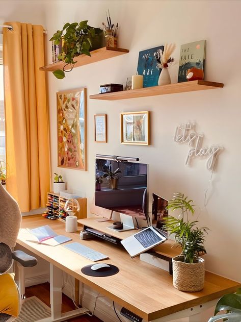 Cozy home office setup featuring a wooden desk under sunlight from a window with yellow curtains. The space is decorated with green plants on floating shelves, motivational posters, and a neon sign saying 'let's play' above the desk. A laptop and monitor provide a functional work area. Creative Workspace Inspiration, Cozy Desk Setup, Cozy Desk, Desk Inspiration, Aesthetic Space, Workspace Inspiration, Home Office Setup, Room Setup, Desk Setup