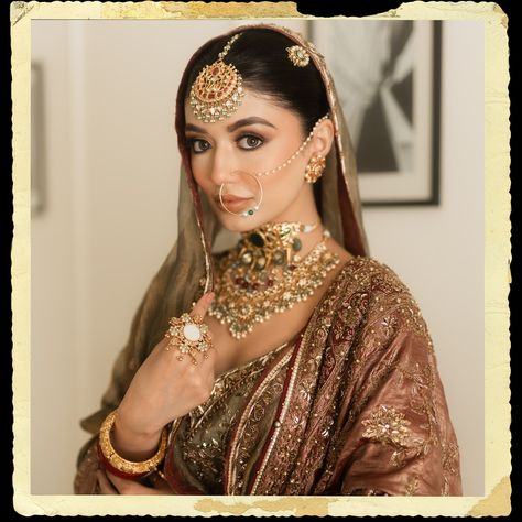 The intricate maang tikka, with its detailed gold work and delicate hanging pearls, graces her forehead, perfectly complemented by the large, ornate nath (nose ring) that adds a classic touch of elegance. Her neck is beautifully accentuated by a layered choker necklace, encrusted with a blend of precious stones and elaborate filigree designs, epitomizing luxury and grandeur. The look is completed with statement earrings, an opulent ring, and a pair of intricately designed bangles, all contrib... Gold Maang Tikka Designs, Maang Tikka Bridal, Nath Design, Nath Bridal, Maang Tikka Design, Choker Outfit, Tikka Designs, Nath Nose Ring, Bridal Nose Ring