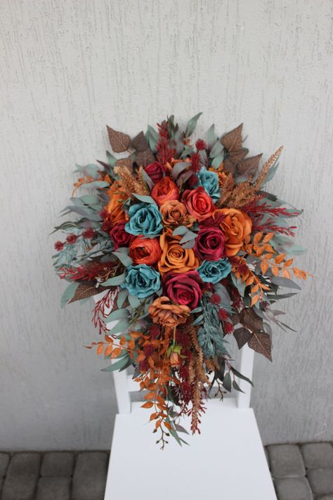 This cascading fall wedding bouquet is a captivating masterpiece, featuring a rich and moody color scheme that marries dark teal, rust, and burgundy flowers. The bouquet's lush design exudes a sense of opulence and warmth, making it an ideal choice for a fall wedding. The deep, luxurious hues of dark teal, rust, and burgundy come together to create a truly dramatic and stunning arrangement, adding a touch of elegance to the autumn celebration. ○ Color: teal, burgundy, rust, brown, green ○ Person Rust Teal Burgundy Wedding, Teal Burnt Orange And Burgundy Wedding, Spring Teal Wedding, Rust Burgundy Wedding, May Wedding Bouquet, Teal And Rust Wedding, Teal And Burgundy Wedding, Dark Teal And Rust Orange Wedding, Teal Fall Wedding