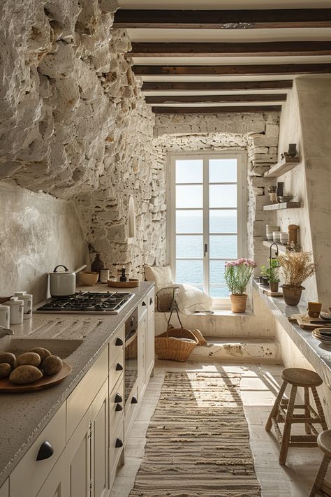 Timeless Coastal Charm in Your Passive Kitchen – This quaint kitchen showcases rough stone walls and exposed wooden beams that exude rustic warmth. A large, grid-patterned window offers stunning sea views and floods the space with natural light. Shelves and potted plants enrich the ambiance. Grupo Reunion expertly blends energy efficiency with design elegance. Imagine living in a space that stays beautiful and relevant for decades. Explore more of our timeless living solutions today. Italian Kitchen Aesthetic, Light Shelves, Quaint Kitchen, Italy Kitchen, Kitchen Rustic, Coastal Kitchen, Stone Walls, Coastal Charm, Italian Kitchen