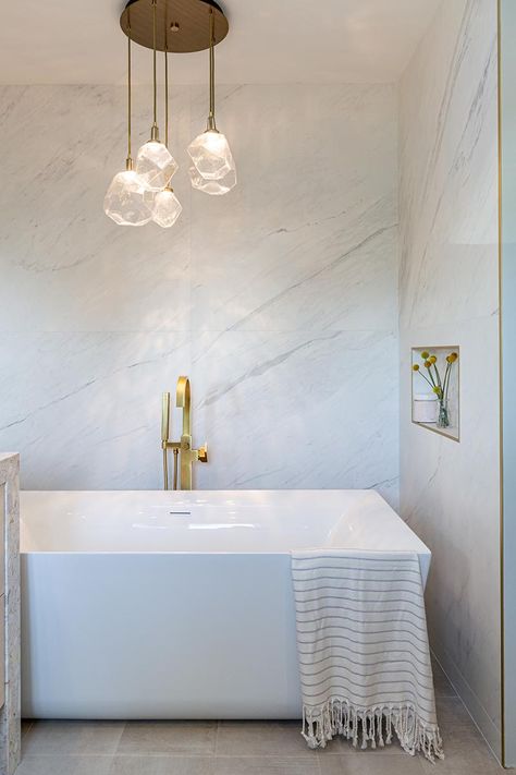 This modern bathroom has a freestanding white bathtub that's recessed into its own alcove. A sculptural multi-light pendant lamps with glass geometric shades, hangs above the bath, highlighting the design. #Bathtub #ModernBathroom Bathtub Lighting, White Bathtub, Bathroom Lighting Design, Brass Shower Head, Bathroom Lights, Bathroom Design Inspiration, Sparkling Lights, Wood Framed Mirror, Bathroom Light