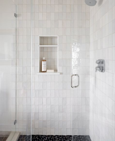 We selected a classic white zellige tile with a textured, natural look placed in a vertical design to give an unexpected look. The shower was grounded with black pebbles to keep it natural. We love the contrast between the two materials.⁠ ⁠ 📸 @mirandaestes Grey Vertical Subway Tile Bathroom, Shower Tile Stacked Horizontal, Textured White Bathroom Tiles, Stacked Subway Tile Shower With Niche, Cloe Tile Vertical Stack, Vertical Shower Niche, White Vertical Stacked Tile, White Subway Vertical Stack, Vertical Subway Tile Bathroom