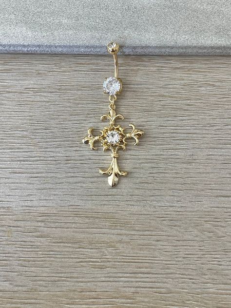 This gold cross belly button ring is beautiful and ornate. Made with surgical steel and coated in 14k gold, this belly button ring dangles with a beautiful cross charm, giving it a gorgeous sparkle, and making it practical for everyday wear. Perfect belly button / navel piercing. Drop jaws with this body jewelry. **PACKAGE INSURANCE: Please either upgrade to priority express shipping at checkout if you would like to insure your package OR you can also purchase insurance separately Insurance up t Gold Cross Belly Button Piercing, Belly Piercing Dangle, Belly Piercing Jewelry Gold, Gold Belly Piercing Aesthetic, Gold Piercings Belly, Belly Ring Gold, Cross Belly Ring, Cross Belly Piercing, Belly Button Piercing Jewelry Gold