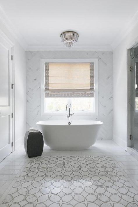 Framed by staggered marble tiles, white and gray marble accent tiles are mounted in front of an oval freestanding bathtub paired with a chrome floor mount tub filler and a black accent stool. Marble Herringbone Bathroom, Herringbone Bathroom, Bathroom Restoration, Marble Bathroom Floor, Marble Herringbone, Standing Tub, Accent Tiles, Bathroom Accent Wall, Wallpaper Bathroom