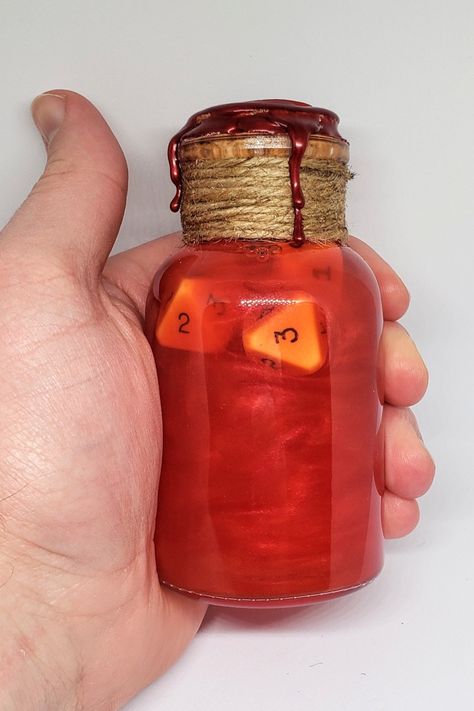 A large glass vial is held in hand. The glass is sealed with cork, twine, and red wax. Inside the glass bottle is a a swirling red liquid and several gaming dice. Potion Dice Roller, Dnd Dice Roller, Dnd Health Potion, Dnd Potions, Potion Of Healing, Potion Maker, Sensory Jars, Lab Decorations, Health Potion