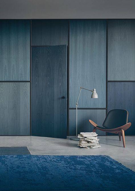 In this blue-hued space by Lissoni Associati Architecture, plywood-stained panels and doors in tone-on-tone muted shades of navy and indigo create the perfect backdrop for a minimalist mid-century display featuring the ever-popular Hans Wegner Shell Chair (interestingly also made out of plywood). Plywood House, درج السلم, Plywood Interior, Interior Design Minimalist, Plywood Walls, Design Room, Hidden Door, Secret Rooms, Design Del Prodotto