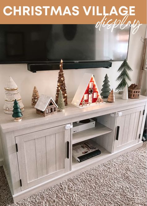 Need a Christmas decor idea for your living room? I created my own little DIY Christmas tree village display on my tv stand this year! The Christmas trees are from all over. The wooden houses are my favorite!! They have candles inside of them. I also found this aframe light up cabin from targets Christmas decor selection and LOVE it! // christmas houses, christmas tree display, christmas decor living room Christmas Decor For Tv Stand, Decorate Tv Stand For Christmas, Christmas Decor Ideas Tv Stand, Christmas Village On Tv Stand, Minimalist Christmas Decor Tv Stand, Tree Village Display, Tv Stand Christmas Decor Ideas, Christmas Entertainment Center Decor, Christmas Decor Tv Stand