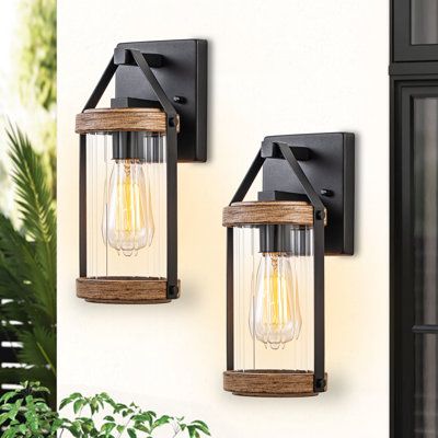 Add rustic charm and warm, welcoming illumination to your outdoor space with these outdoor wall sconces. Inspired by a traditional gas lantern, the light fixture features a clear cylinder-striped glass shade surrounded by a frame hung on the arm. The two-tone powder-coated black and woodgrain finish highlights the beauty of this traditional design. It exudes a vintage appeal that could be easily enhanced by an Edison bulb (not included). Ideal enhancement for traditional homes as well as modern- Modern Wall Scones, Farmhouse Sconces, Wall Sconces Farmhouse, Farmhouse Wall Lighting, Porch Light Fixtures, Farmhouse Wall Sconces, Front Porch Lighting, Wall Sconces Living Room, Exterior Light Fixtures