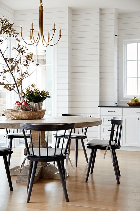 Black spindle chairs sit around a round brown dining table lit by a brass chandelier. Black Spindle Chairs, Spindle Chairs, Black Round Dining Table, Black Leather Dining Chairs, Spindle Chair, Brass Dining Table, Dallas Interior Design, Brown Dining Table, Round Dining Tables