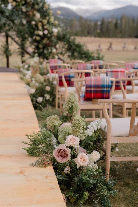 A rustic outdoor wedding ceremony aisle featuring blush-toned floral arrangements, wooden platform, and tartan blankets draped over chairs, creating a warm and inviting atmosphere. Wedding Decor Rustic Chic, Wedding Aisle Floral, Outdoor Wedding Aisle, Floral Ceremony, Wedding Ceremony Setup, Wedding Aisle Outdoor, Romantic Rustic Wedding, Rustic Wedding Ceremony, Blush Wedding Flowers