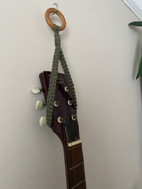 Green guitar or ukulele hanger, ukulele hook, music home decor, ukulele strap, ukulele wall mount, ukulele accessories Wall hanging instrument storage hook made from avocado green recycled cotton on a repurposed wooden hanging ring.  Instrument not included.  One universal size, total length from ring to bottom of loop is approximately 30cm. This simple hanging loop will fit multiple types of string instrument including guitars and ukuleles, but custom orders to fit your specific measurements or Crochet Ukulele Hanger, Guitar And Ukulele On Wall, Macrame Ukulele Hanger Tutorial, Crochet Ukulele Strap, How To Hang Guitars On The Wall, Guitar Holder Wall Diy, Guitar Hanging On Wall, Crochet Ukulele, Crochet Guitar Strap