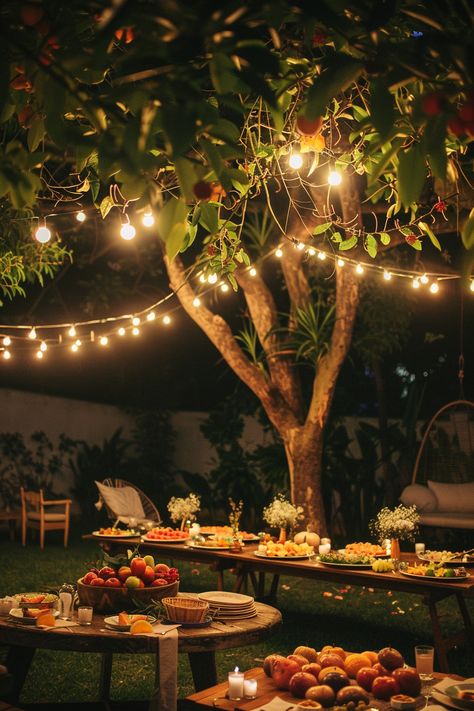 String lights hanging from a tree illuminate an outdoor dining setup with tables filled with assorted fruits and food, creating a cozy evening ambiance. Backyard Potluck Wedding, Outdoor Backyard Party Ideas, Backyard Dinner Party Food, Barbecue Theme Party Ideas, Aesthetic Outdoor Party, Cute Backyard Wedding Ideas, Summer Backyard Engagement Party, Backyard House Party, Backyard Gathering Ideas