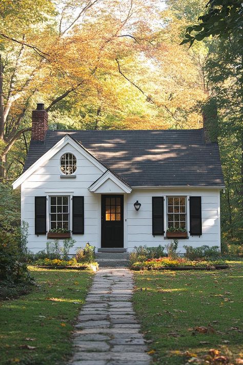 Small white cottage with black shutters and a gabled roof surrounded by fall foliage. One-story homes, where you can skip the stair workout and enjoy open, airy spaces with a side of charm. Steep Pitch Roof Cottage, House Without Front Porch, Small White House With Shutters, White Cottage Black Shutters, Small Country House Exterior, White One Story House, One Story Cottage Exterior, Tiny Colonial House, Cottage Style Exterior Homes