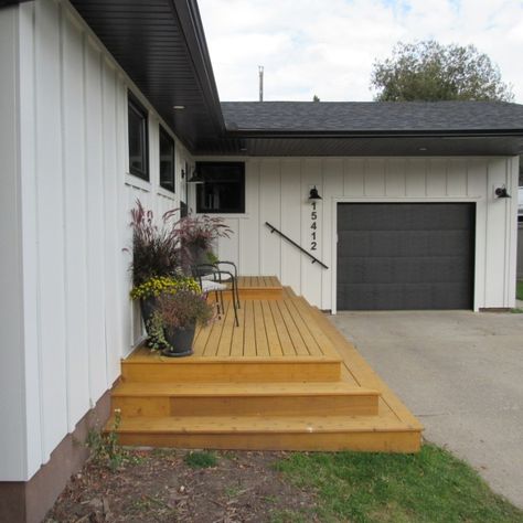 We replaced the existing wood siding with Arctic White Hardie Plank and Panel in a board and batten style, as well as black soffit/fascia/eaves. The new black windows, front door, and gorgeous stained deck all tie in to a perfectly designed modern farmhouse exterior. Vertical Hardie Board Siding Modern Exterior, White Board And Batten Ranch House, Sofits And Facias Exterior, White Vertical Siding Exterior Ranch, Black Eaves Exterior, Hardy Board Siding Ideas, Modern Board And Batten Exterior, Wood Fascia And Soffit, Black Soffit And Fascia White House