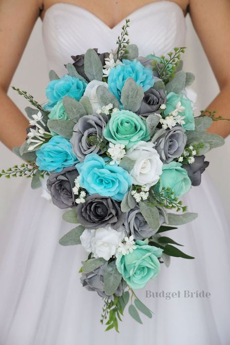 This lovely assortment of mint, spa, gray and white roses is bound to turn heads on your wedding day. This lovely cascading brides’ bouquet from the is an absolutely breathtaking arrangement for any bride to be, in any season. Sage greenery and white accents complete the look and add a delicate realism to this beautiful bouquet. This bouquet is 10” wide, 18” long, and is crafted by our in-house florists without using a foam base to anchor the flowers to the bouquet. Instead, we wire our bouquets Sage Green Accents, Turquoise Bouquet, Small Bridesmaid Bouquets, Fake Wedding Flowers, Gray Roses, Wedding Strawberries, Sage Eucalyptus, Fresh Wedding Flowers, Grey Wedding Dress