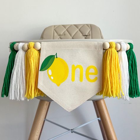 A lemon party for your little one who is turning a year old, this 1st birthday highchair banner is the perfect flag to celebrate a milestone birthday. An adorable banner for your main squeeze, a fun yellow lemon with green leaves makes the O followed by a yellow NE to spell one. This makes this flag a classic for your little one's first celebration.  Banner includes 6 tassels in yellow, white and green separated by wooden beads. Hang on a high chair or above the cake table and when the party is over hang on the wall as part of a room decoration.  This cake smash sign makes an awesome photo prop and keepsake. You have the option to add the ONE gold glitter cake topper.  Add a matching lemon balloon from our sister store https://www.etsy.com/listing/972521733 Add a custom lemon birthday bann