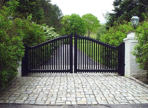 A transitional-style driveway gate features the arch and pickets of a traditional entry gate, but with a black finish and contrasting white brick pillars that update the look. Gate designed and installed by Tri State Gate in Bedford Hills, New York. Farm Gates Entrance, Iron Gates Driveway, Entrance Gates Driveway, Wood Gates Driveway, Gate Driveway, Metal Driveway Gates, Driveway Entrance Landscaping, Wooden Gates Driveway, Black Gate