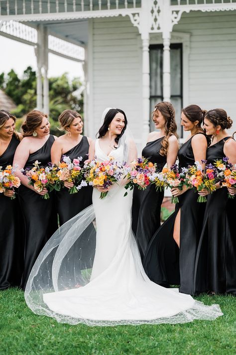 Bride with bridesmaids in black gowns with colorful bouquets Black With Wildflowers Wedding, Black And White Weddings With A Pop Of Color, Black Bridesmaid Dresses Colorful Shoes, White Wedding Bouquets With Pop Of Color, Black With Bright Colors Wedding, Black Wedding With Bright Flowers, Black And White Wedding With Colored Flowers, Black Bridesmaid Dresses With Wildflowers, Black Bridesmaid Dresses With Bright Bouquets