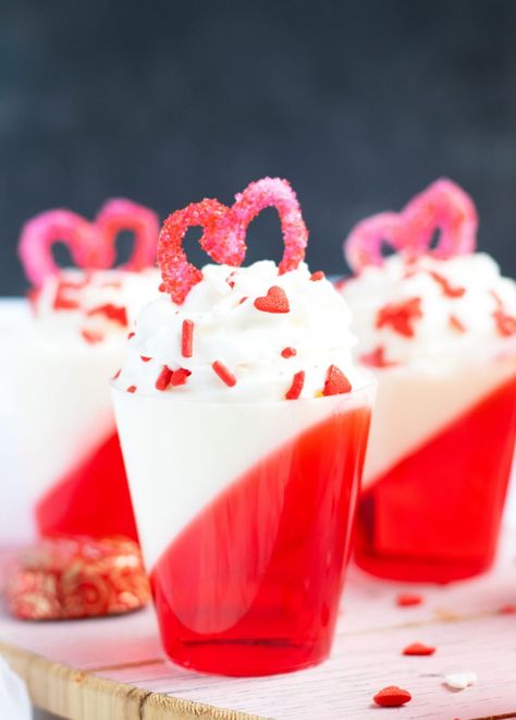 These Strawberries and Cream Layered Jell-O shots are a festive Valentine's Day treat with whipped cream vodka.  A heart made out of melted white chocolate and sugar sprinkles makes the perfect topper. Strawberry Cream Jello Shots, Jello Shots Valentines Day, Canada Day Jello Shots, Red And White Jello Shots, Valentines Day Jello Shots, Valentine’s Day Jello Shots, Valentine Jello Shots, Valentines Shots, White Jello Shots