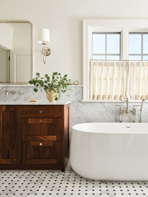 The tranquil primary bath focuses on refined finishes, such as the Carrara marble slab wainscoting and marble mosaic flooring from The Tile Shop. A freestanding Kohler Ceric tub with a wall-mounted Waterworks faucet anchors the space. Waterworks Faucet, Bathroom Wainscoting Ideas, Carrara Marble Bathroom, Brass Shelving, Handmade Stool, Wainscoting Bathroom, Marble Tile Bathroom, Wall Mount Tub Faucet, Primary Bath