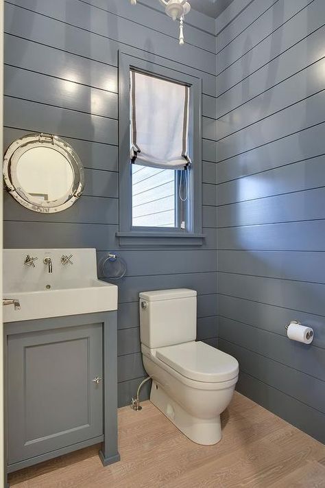 Blue cottage powder room boasts blond oak wood floors framed by blue shiplap walls and is fitted with a white porcelain toilet positioned beneath a window dressed in a gray grosgrain roman shade. Bathrooms With Shiplap, Fixer Upper Bathrooms, Shiplap Powder Room, Cottage Powder Room, Blue Shiplap, Shiplap Bathroom Wall, Blue Walls Living Room, Vertical Shiplap, Farmhouse Bathroom Decor Ideas