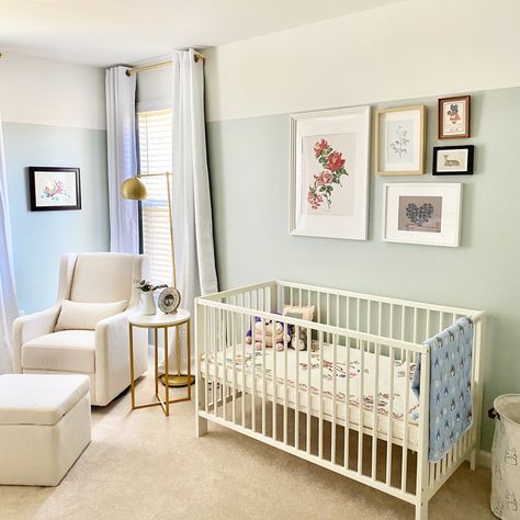 Nursery with pale green/gray walls, a gallery wall with a large pink flower painting and other nature inspired art above the white Ikea crib, a cream rocker/glider in the corner of the room in front of a window with white curtains, a gold and marble side table and a modern vintage floor lamp next to the glider. Sea Salt Nursery, Ikea Gulliver Crib, Sherwin Williams Sea Salt, Modern Girl Nursery, Rocker Glider, Nursery Nook, Sea Salt Sherwin Williams, Virtual Baby Shower, Big Boy Room