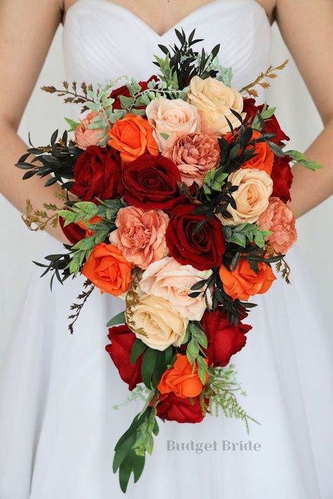 This lovely assortment of red, orange, champagne and sand colored roses is bound to turn heads on your wedding day. This lovely cascading brides’ bouquet from the is an absolutely breathtaking arrangement for any bride to be, in any season. Bright greenery and dusty peach peony accents complete the look and add a delicate realism to this beautiful bouquet. This bouquet is 10” wide, 18” long, and is crafted by our in-house florists without using a foam base to anchor the flowers to the bouquet. I Red And Orange Wedding Decorations, Fall Color Bouquet, Brick Red Wedding Colors, Orange And Red Wedding Flowers, Mexican Style Wedding Bouquet, Mexican Wedding Flowers Bridal Bouquets, Red And Orange Wedding Theme, Red And Orange Bouquet, Sunset Wedding Flowers