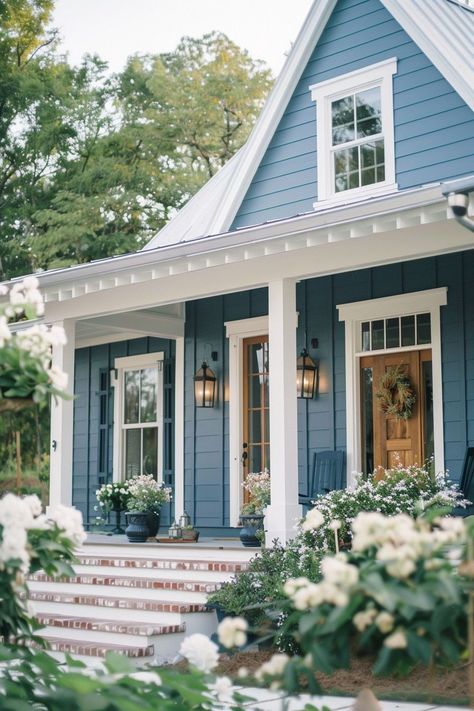 I love using blue paint for home exteriors because it has a versatile and refreshing appeal. The color blue offers a wide range of shades, from soft pastels to bold, vibrant hues, allowing for a diverse array of design options. Whether it's a light, sky blue for a cottage-style home or a dark, moody navy for a modern look, blue paint can be tailored to suit a variety of architectural styles and personal preferences. Natural Shingle House Exterior, Blue Farmhouse Exterior White Trim, Blue And Grey House Exterior, Small Blue House Exterior, Chic Exterior House Colors, Best Farmhouse Exterior Paint Colors, Blue House Porch Decor, Blue Roof White House, Cottage Colors Exterior Colour Schemes