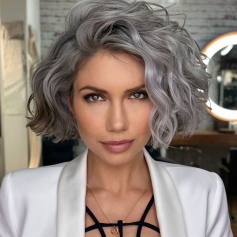 This curly silver bob is the perfect fall haircut for embracing natural greys with a modern twist. The voluminous curls add softness and elegance, making it ideal for a polished, sophisticated appearance this season. Perfect for those who want to highlight their natural beauty in a stylish, effortless way. Wavy Gray Bob, Silver Blonde Curly Hair, Gray Curly Bob, Grey Curly Hair Natural Curls, Curly Bob Grey Hair, Wavy Grey Bob, Silver Wavy Bob Hairstyles, Curly Grey Shag Haircut, Silver Bob