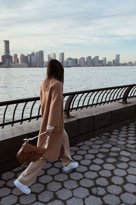 New york city based fashion influencer Lauren Lora wearing a neutral monochrome outfit. She’s wearing a camel wool coat, beige wide leg pants, white sneakers and a brown dior saddle bag. Brown Saddle Bag Dior, Brown Saddle Bag Outfit, Dior Saddle Brown, White Dior Saddle Bag Outfit, Brown Bag Outfit Winter, Brown Bag Outfit, Edge Outfits, Dior Saddle Bag Outfit, Taupe Outfit