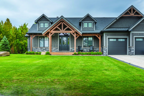 Timbers, shingles, stone and grey siding combine a welcoming exterior. Where To Put Stone On A House Exterior, Grey Wood House Exterior, Houses With Grey Siding, Grey Siding With Wood Accents, Grey Shingles House, Grey And Stone House Exterior, Slate Grey Exterior House Color, Modern Farmhouse Bungalow Exterior, Grey Home Exterior With Stone