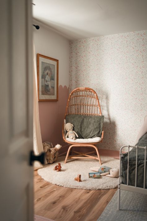 Photo features a open, the door peeking into a children’s bedroom with a rattan chair in a corner with toys on the floor. The corner of a bed is shown floral wallpaper on one wall and dusty rose pink scallop wall on the other wall with a vintage painting of two sisters under a floral arch on the scalloped wall. White rug on hardwood floor. Dusty Rose Toddler Room, Dusty Rose And Green Nursery, Bedroom Dusty Rose, Green Girls Room, Dusty Rose Nursery, Shared Toddler Room, Girls Bedroom Green, Pink Playroom, Green Girls Rooms