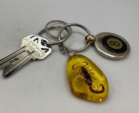 Step into the world of ancient wonders with this exquisite Scorpion in Amber Resin Keychain. Crafted with precision, this keychain features scorpion encased in high-quality amber resin, offering a glimpse into a prehistoric era. The warm, golden hues of the resin beautifully encapsulate the scorpion, creating a mesmerizing effect that is both captivating and elegant. This keychain is not only a functional accessory but also a miniature piece of art that showcases the intriguing beauty of nature. This keychain is more than just a decorative item; it symbolizes strength, protection, and resilience, attributes often associated with scorpions in various cultures. The amber resin adds a touch of ancient mystique, as amber has been prized since antiquity for its color and natural beauty. Lightwe 90s Keychains, Scorpion Keychain, Bug Keychain, Lighter Keychain, Creative Keychains, Fun Keychains, Cool Keychain, Arizona Gifts, Edc Keychain