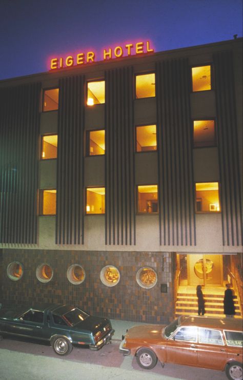 Photography of a hotel entrance with cars upfront, yellow lit room light and a neon sign 70s Hotel Aesthetic, 60s Hotel, Dystopian Book, 70s Architecture, Retro Hotel, Miami Hotel, Dream Hotel, Background References, Business Architecture