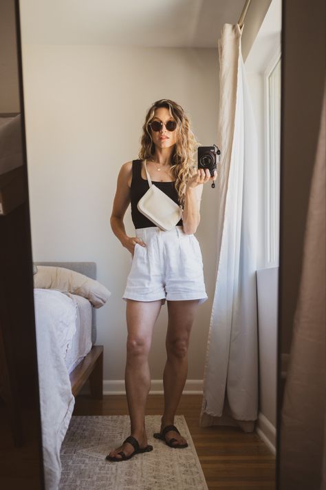 Ashley wearing a black tank, white linen shorts, black sandals, a beige belt bag, and tortoiseshell sunglasses Outfit With Linen Shorts, Linen White Shorts Outfit, Olive Linen Shorts Outfit, White Shorts Black Top Outfit, Styling Linen Shorts, White Short Outfits Summer, Cream Linen Shorts Outfit, Black Sandals Outfit Casual, Summer Linen Shorts