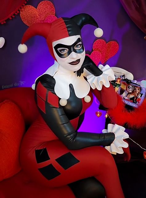 A cosplayer in a classic Harley quinn cosplay. A red and black skin tight jester outfit. Sitting on a short red velvet chair, one elbow propped up on a side table, and her chin rests against her hand. On the table is a vintage white phone, a photo frame with Harley and ivy inside, and red marabou feathers. Hearts and red sheer curtains adorn a purple backdrop behind the cosplayer. Jester Harley Quinn, Harley Cosplay, Woman In Love, Harley Quinn Artwork, Harley Quinn Costume, Clubbing Outfits, Bruce Timm, Batman The Animated Series, Joker Cosplay