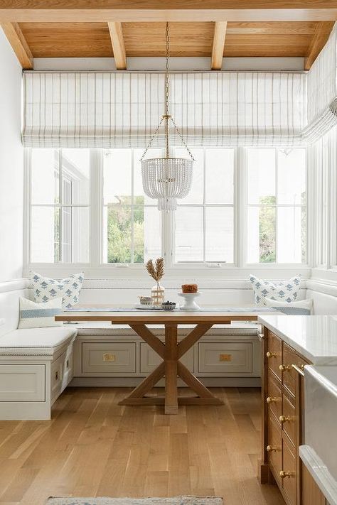 Hung from a brown wood plank ceiling over a square trestle dining table, a white beaded chandelier lights a breakfast nook finished with a built-in u-shaped dining bench. White Beaded Chandelier, Tan Dining Chair, Latest Kate, Designers Portfolio, Neutral Interior Design, Wood Plank Ceiling, Kate Marker Interiors, Plank Ceiling, Transitional Dining Room