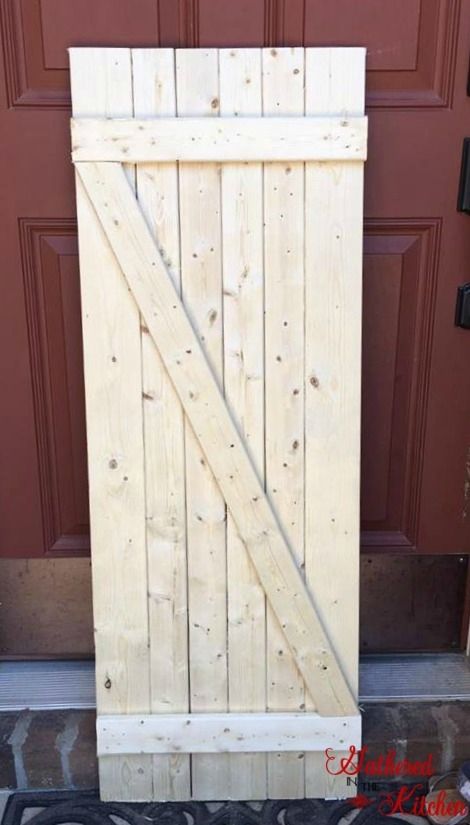 wooden barn door, unstained, leaning against a red exterior door Diy Barn Door Cheap, Barn Door Diy, Reban Ayam, Exterior Barn Door, Exterior Barn Doors, Wooden Barn Doors, Family Room Walls, Diy Barn, Door Diy