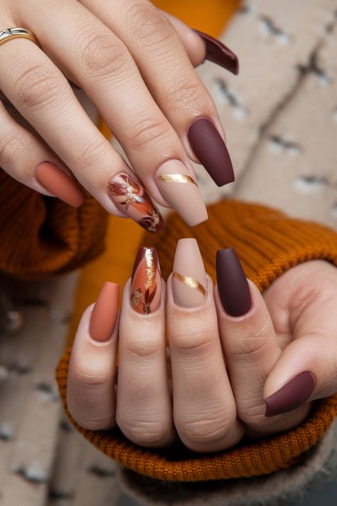 Embrace the beauty of autumn with these stunning coffin-shaped fall nail ideas. Featuring rich hues of burgundy and burnt orange along with delicate gold accents, this nail style captures the essence of the season perfectly. Whether you're dressing up for a pumpkin spice outing or simply showcasing your seasonal spirit, these nails are the ideal statement. Get inspired for your next manicure! Fall Nails Browns And Oranges, Orange And Tan Nails, Orange And Burgundy Nails, Fancy Fall Nail Designs, Orange Nail Design Ideas, Burgundy Autumn Nails, Coffin Autumn Nails, Matte Burnt Orange Nails, Gold Autumn Nails