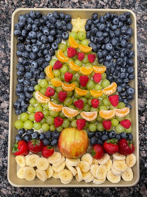 A colorful christmas tree shaped fruit platter on a silver baking tray. A star fruit slice forms the star on top of the tree, and mandarin oranges are strung together like streamers going around the tree.