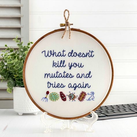 What doesn't kill you mutates and tries again. Finished and framed, this quirky embroidery hoop art is ready to hang or gift to the microbiologist in your life. Featuring detailed microbes(virus, bacteriophage, etc.) a scientist will appreciate the detailed stitching as well as a modern cool toned color palette of thread colors. This completed artwork is about 7 inches in diameter, so it works hung standalone on a wall or displayed on a shelf with other unique keepsakes. Free gift wrapping & a p Cool Toned Color Palette, Quirky Embroidery, Funny Embroidery, Science Teacher Gifts, Funny Science, Nerdy Gifts, Framed Embroidery, Cross Stitch Finishing, Science Gifts