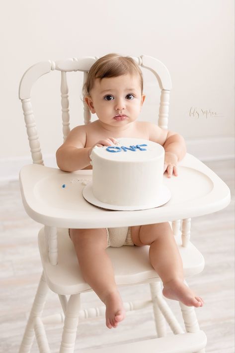 One-year-old boy touches the frosting of his First Birthday Cake as he sits in an antique white high chair during a Cake Smash Session by Lily Sophia Photography near the Decatur area of Atlanta, Georgia. White Cake Smash Photoshoot, Wooden High Chair Cake Smash, All White Smash Cake Photos, Antique High Chair Cake Smash, White Balloon Cake Smash, Milestone Photography, Chair Pictures, Natural Light Studio, Expecting A Baby