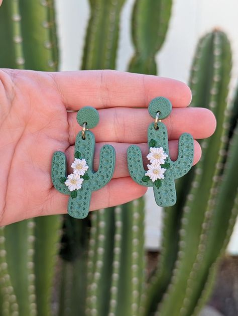 Handmade Polymer Clay Earrings: Saguaro Cactus Dangles with Blooming Flowers! Created locally in the Coachella Valley, Southern California Desert. *Hypoallergenic *Gold finish glued-on posts *BOTH rubber backing and soft close backing provided *Lightweight and extra comfortable *Entirely handmade This design is *Made to order*. All clay creations are completely handmade and will differ slightly from the photos shown. Please handle with care. Avoid direct contact with dirt and water. Please feel Mexican Style Clay Earrings, Texas Clay Earrings, Clay Cactus Earrings, Polymer Clay Cactus Earrings, Cactus Polymer Clay Earrings, Clay Experiments, Polymer Clay Cactus, Cactus Clay, Clay Cow