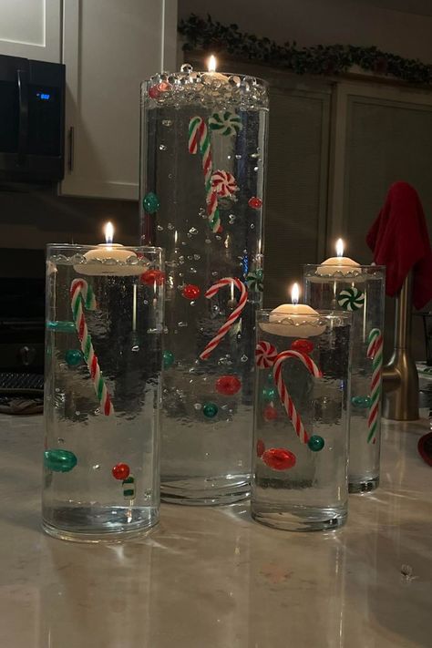 Orbeez Christmas vase with floating candles on top. Inside the four vases the decorations appear to float due to clear orbeez decor. There are candy canes and green and red ornaments in the vases for a Christmas centerpiece. Orbeez Christmas Decor, Floating Candles Christmas, Unique Christmas Decorations Diy, Diy Orbeez, Christmas Floating Candles, Water Beads Centerpiece, Diy Christmas Vases, Floating Candle Centerpieces Diy, Christmas Centrepiece Ideas