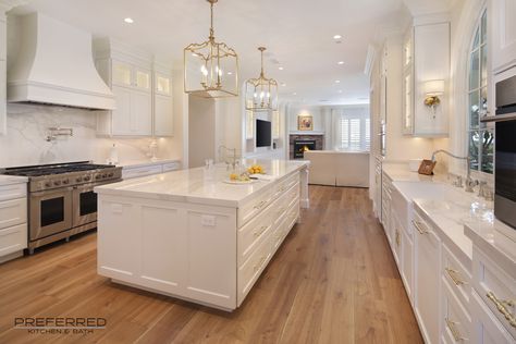 White gorgeous kitchen with golden wood floors that match the gold accents in the space created by the pendants and hardware. White And Golden Kitchen Modern, Kitchen Ideas White And Gold, Kitchen Wood Flooring Ideas White Cabinets, White And Golden Kitchen, White Kitchen Gold Accents, White Kitchen With Wood Floors, White Kitchen Gold Hardware, White Kitchen With Gold Hardware, White And Gold Kitchen Ideas