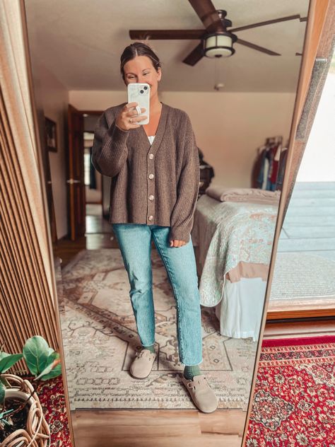 Girl standing in front of mirror in brown cardigan, blue jeans, green socks and taupe clogs Oversized Button Cardigan Outfit, Chocolate Cardigan Outfit, Brown Short Cardigan Outfit, Short Brown Cardigan Outfit, Dark Brown Cardigan Outfit, Brown Cropped Cardigan Outfit, Brown Cardigan Outfit Aesthetic, Button Up Cardigan Outfit, Brown Clogs Outfit